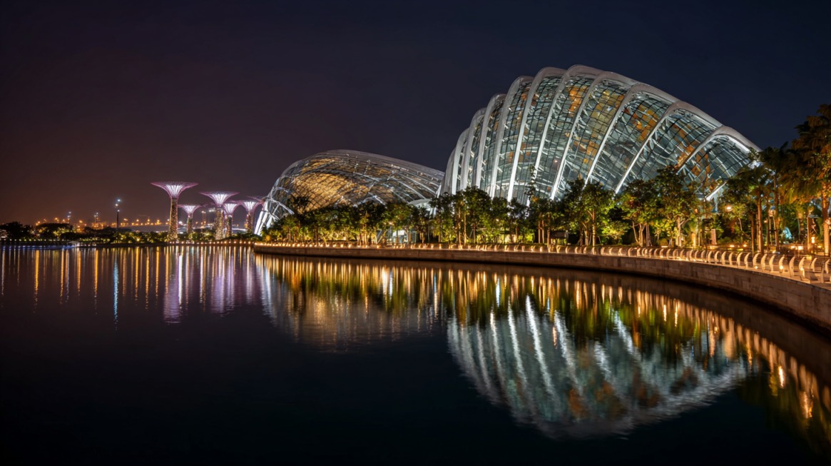 Night view of Gardens by the Bay in Singapore with illuminated Supertrees and glass conservatories reflected in calm waters