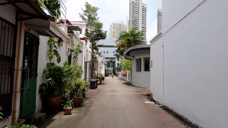 Narrow alley with low-rise houses, greenery, and modern towers in the background in Tiong Bahru