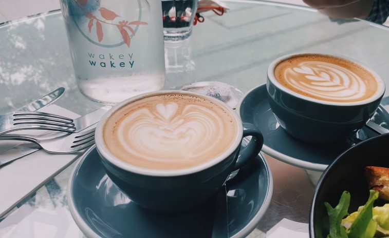 Two perfectly poured lattes on a restaurant's glass table