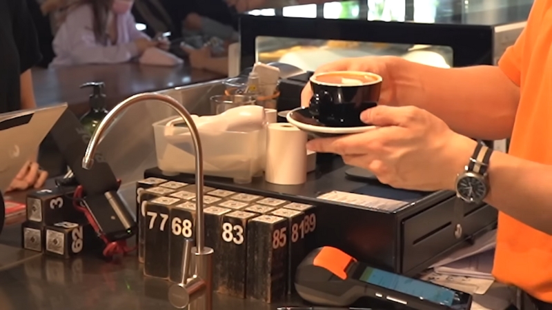 A kopi uncle at a Singapore coffee stall serves a cup of coffee while managing multiple customer orders