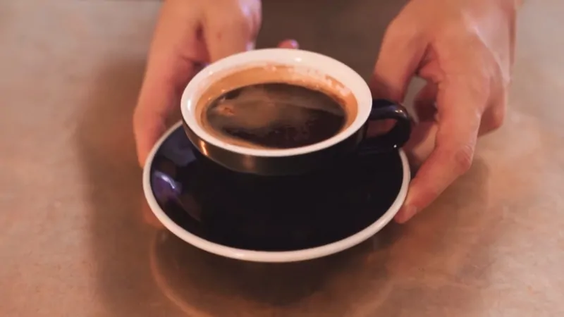 A cup of traditional Singaporean kopi served black in a dark ceramic cup on a saucer