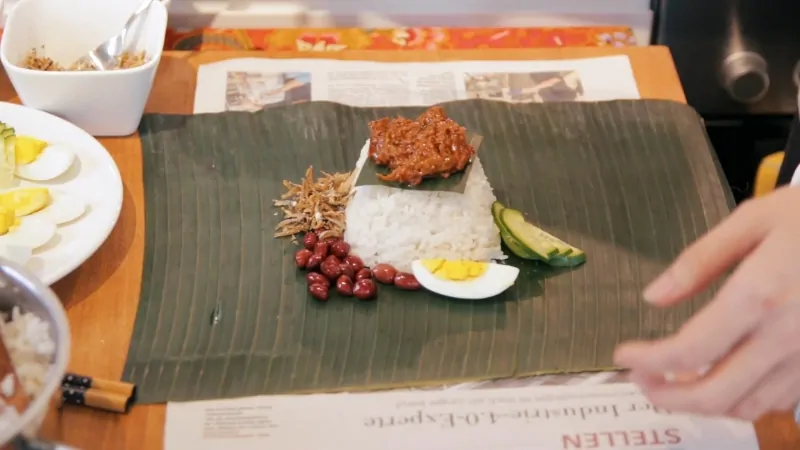 A serving of nasi lemak prepared on a banana leaf with rice, sambal, egg, peanuts, and anchovies