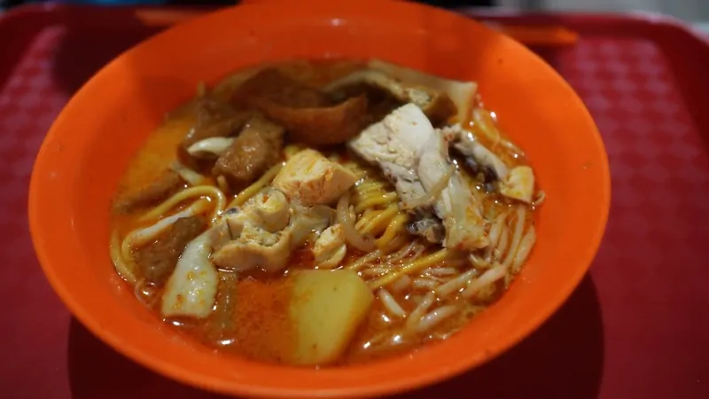 A bowl of curry noodles in a Singapore wet market filled with fresh noodles, chicken, and rich broth