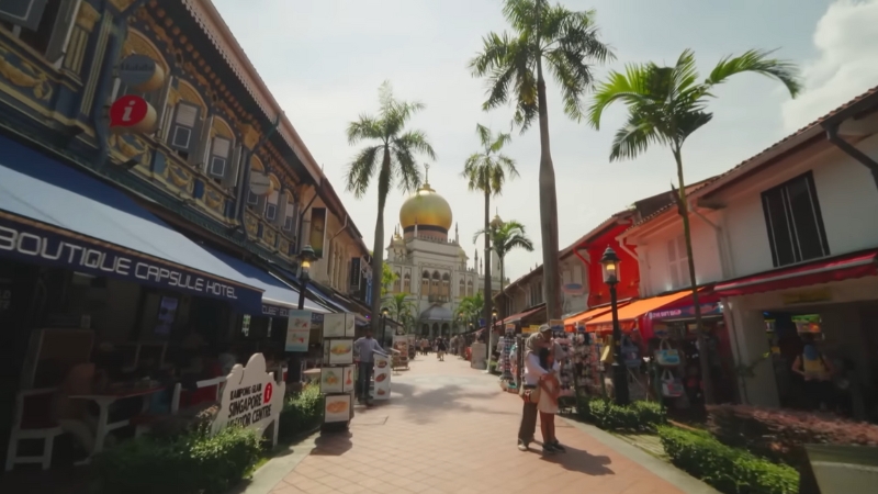 A sunny street view of Kampong Glam with palm trees, shophouses, and the Sultan Mosque in the distance