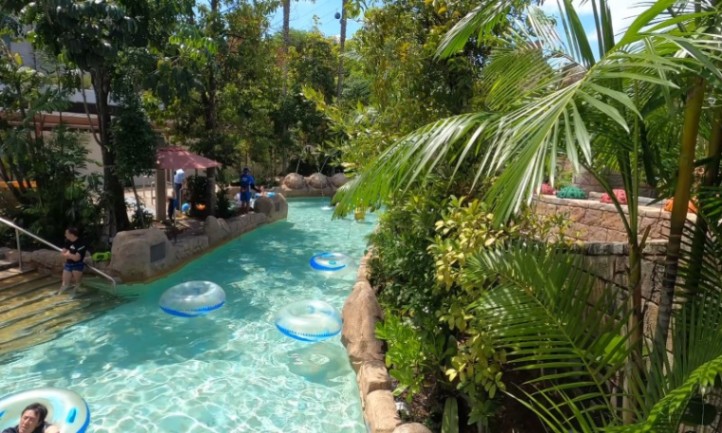 A lush, tropical lazy river with clear water and floating inner tubes
