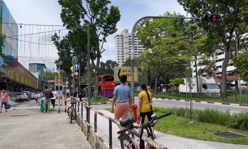 A bustling urban street scene with pedestrians walking, a red bus approaching, and bicycles parked near a railing