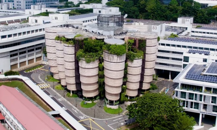 Aerial view of a unique, cylindrical green building with lush rooftop gardens
