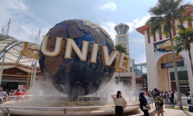 A large, rotating globe with "UNIVERSAL" in bold letters sits amidst mist at a theme park entrance