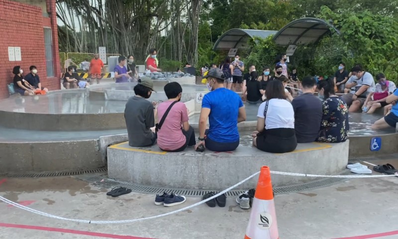 People seated around a steaming hot spring in a park