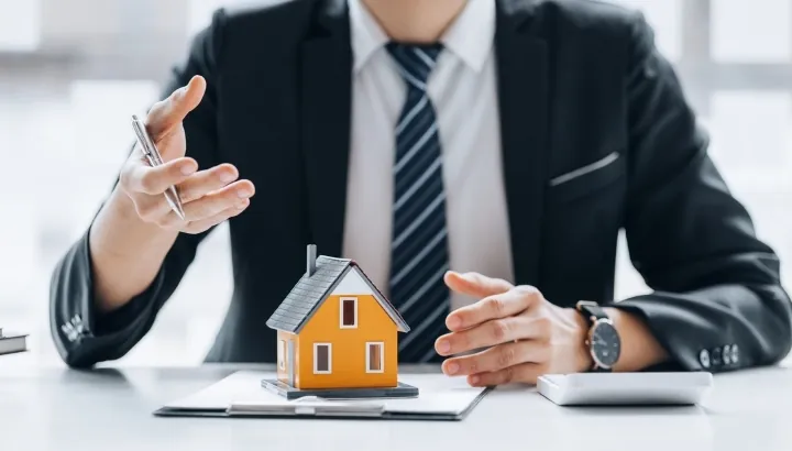 Real estate adviser in a business suit discussing property ownership with a miniature house on the desk.
